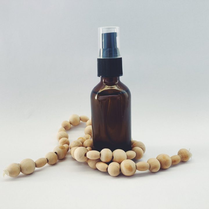 Glass bottle of DIY cleansing oil with wooden beads wrapped around it on a white background.
