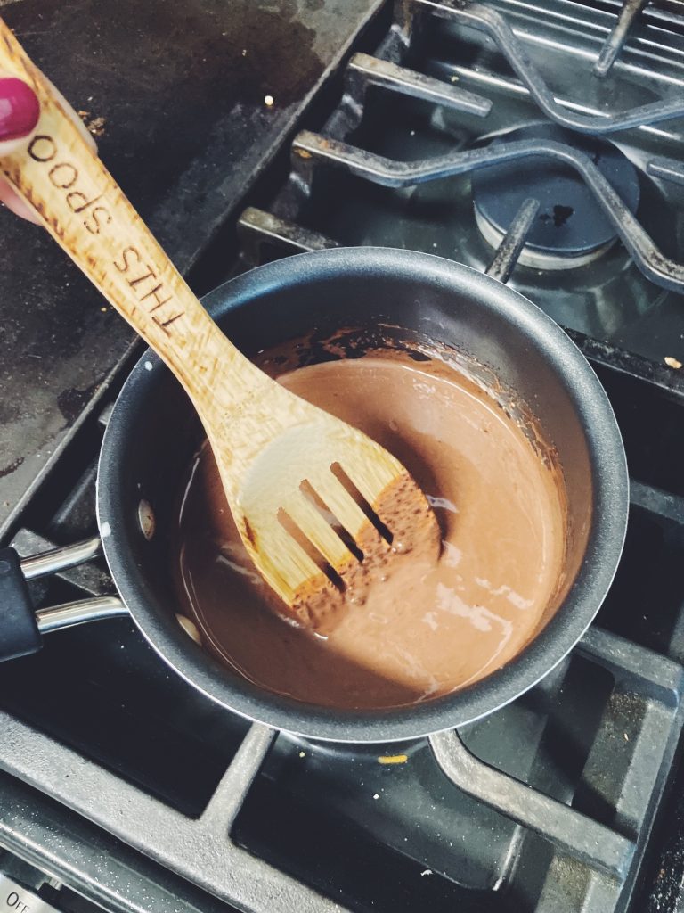 Spoon stirring a pot of drinking chocolate on the stove.