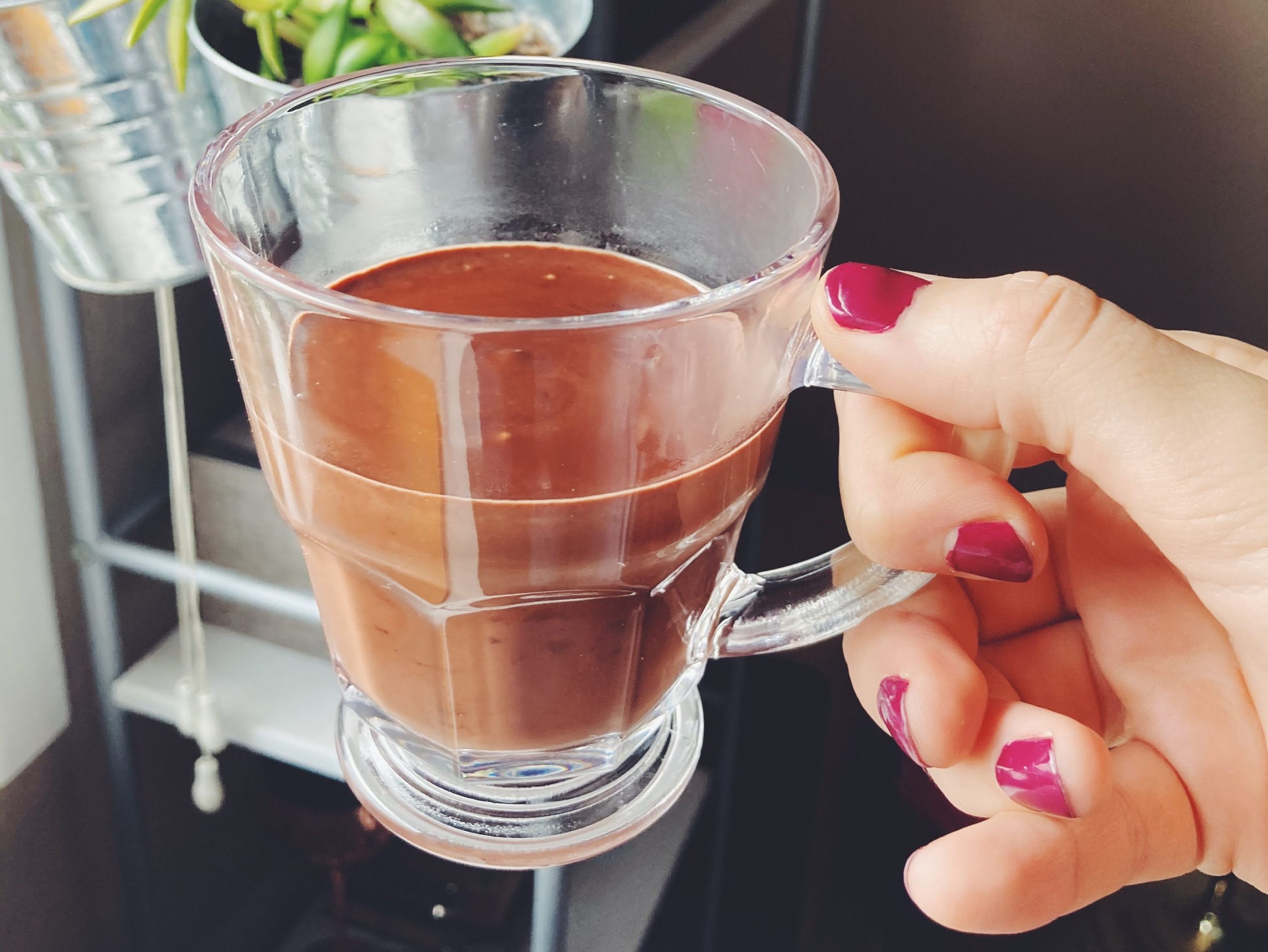 Hand holding a mug of drinking chocolate in a clear glass.