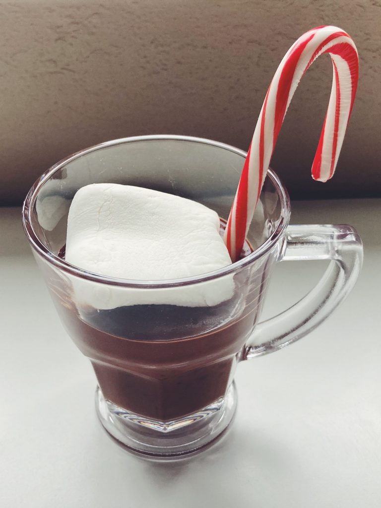 Glass mug with drinking chocolate and a large marshmallow and a candy cane.