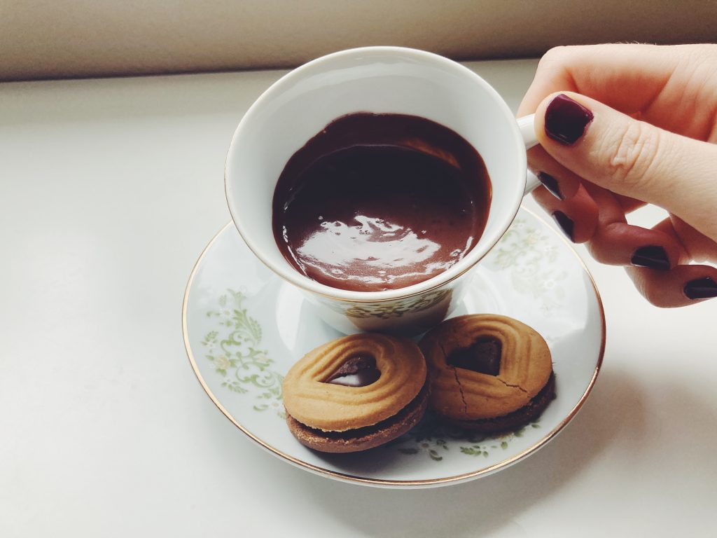 Teacup of drinking chocolate with two cookies next to it being tilted to sip.