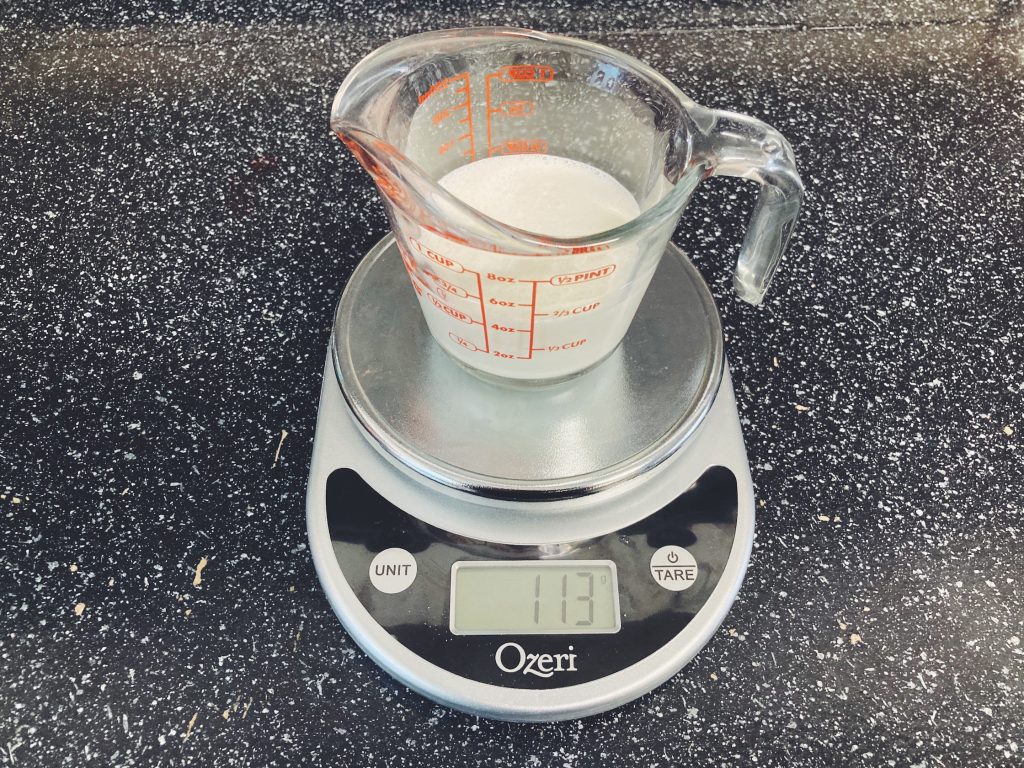Heavy cream in a measuring cup on a kitchen scale.