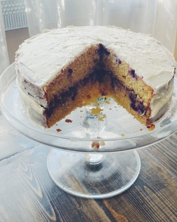 Photo of a blueberry lemon einkorn cake with a slice cut out on a cake stand