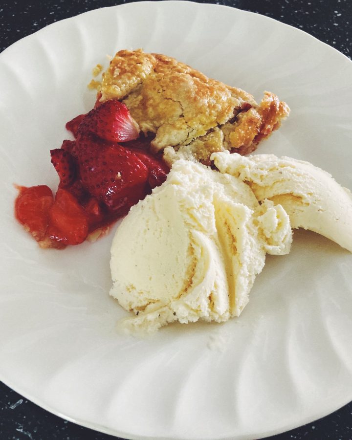 Deliciously red einkorn crust strawberry galette with a scoop of vanilla ice cream on a white plate.